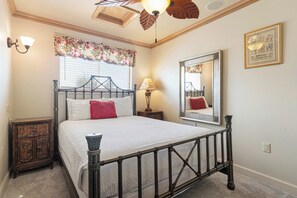 Quarto com cama, mesa de cabeceira, luminária, espelho e janela com persianas.