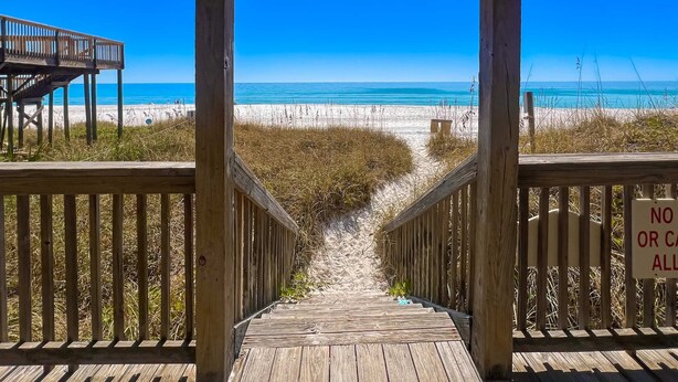 Un paseo marítimo de madera que conduce a una playa con vista clara al océano.