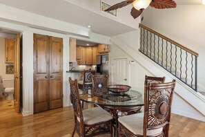 A dining area with a glass table surrounded by wicker chairs, a kitchen with wooden cabinets and a refrigerator, and a staircase with a metal railing. - Beach Condo with Free WiFi, Washer/Dryer, Beach Service Now Included (Miramar Beach)