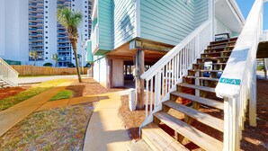 Una escalera de madera que conduce a un edificio con un cartel que dice '6-A', rodeada de un césped bien cuidado y un edificio residencial alto al fondo.