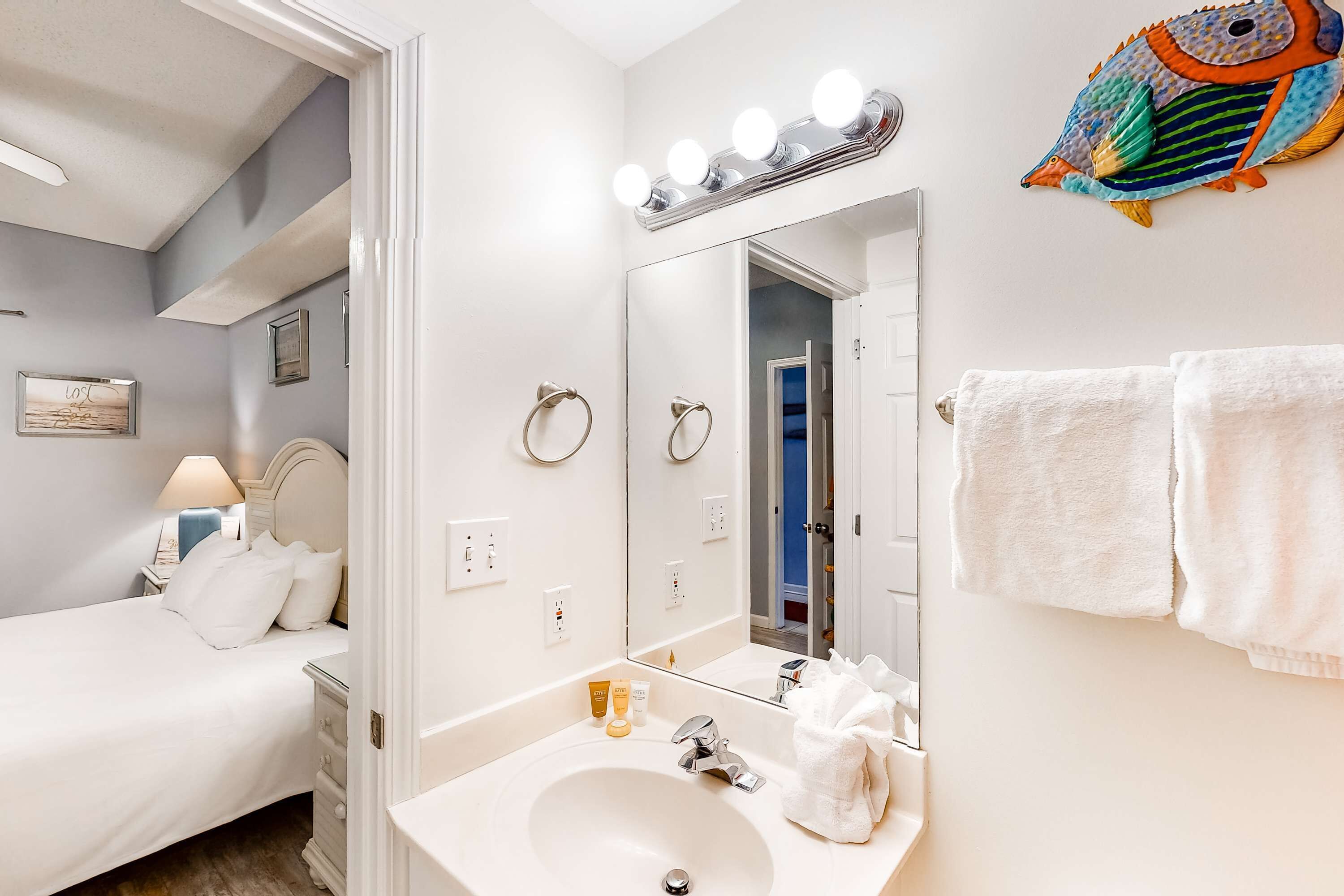 Un baño de hotel con un espejo grande, tocador y una cama en la habitación contigua.