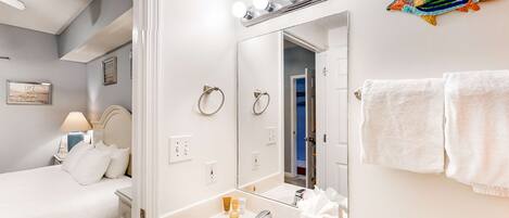 Un baño de hotel con un espejo grande, tocador y una cama en la habitación contigua.