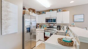 A modern kitchen with white cabinets, stainless steel appliances, and decorative items on the countertops. - Pet-friendly, pools, hot tub & balcony with Gulf-side calm (Destin)