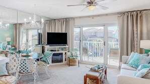 A spacious living room with a large flat-screen TV, a ceiling fan, and a balcony with a view. - Pet-friendly, pools, hot tub & balcony with Gulf-side calm (Destin)