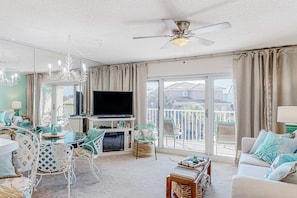 A spacious living room with a large flat-screen TV, a ceiling fan, and a balcony with a view. - Pet-friendly, pools, hot tub & balcony with Gulf-side calm (Destin)