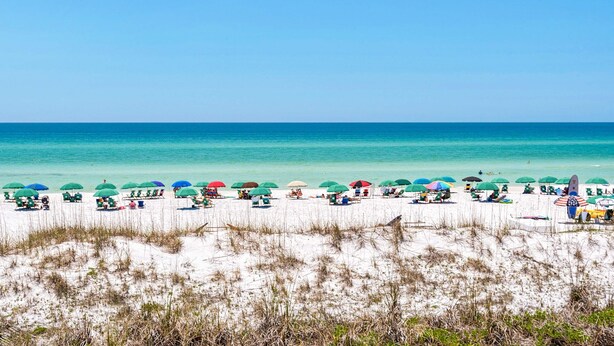 A beach with rows of beach umbrellas and chairs, a clear blue sky, and the ocean in the background. - Pet-friendly, pools, hot tub & balcony with Gulf-side calm (Destin)