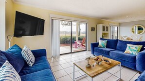 Uma sala de estar com um sofá azul, uma mesa de centro de madeira e uma televisão de tela plana fixada na parede.