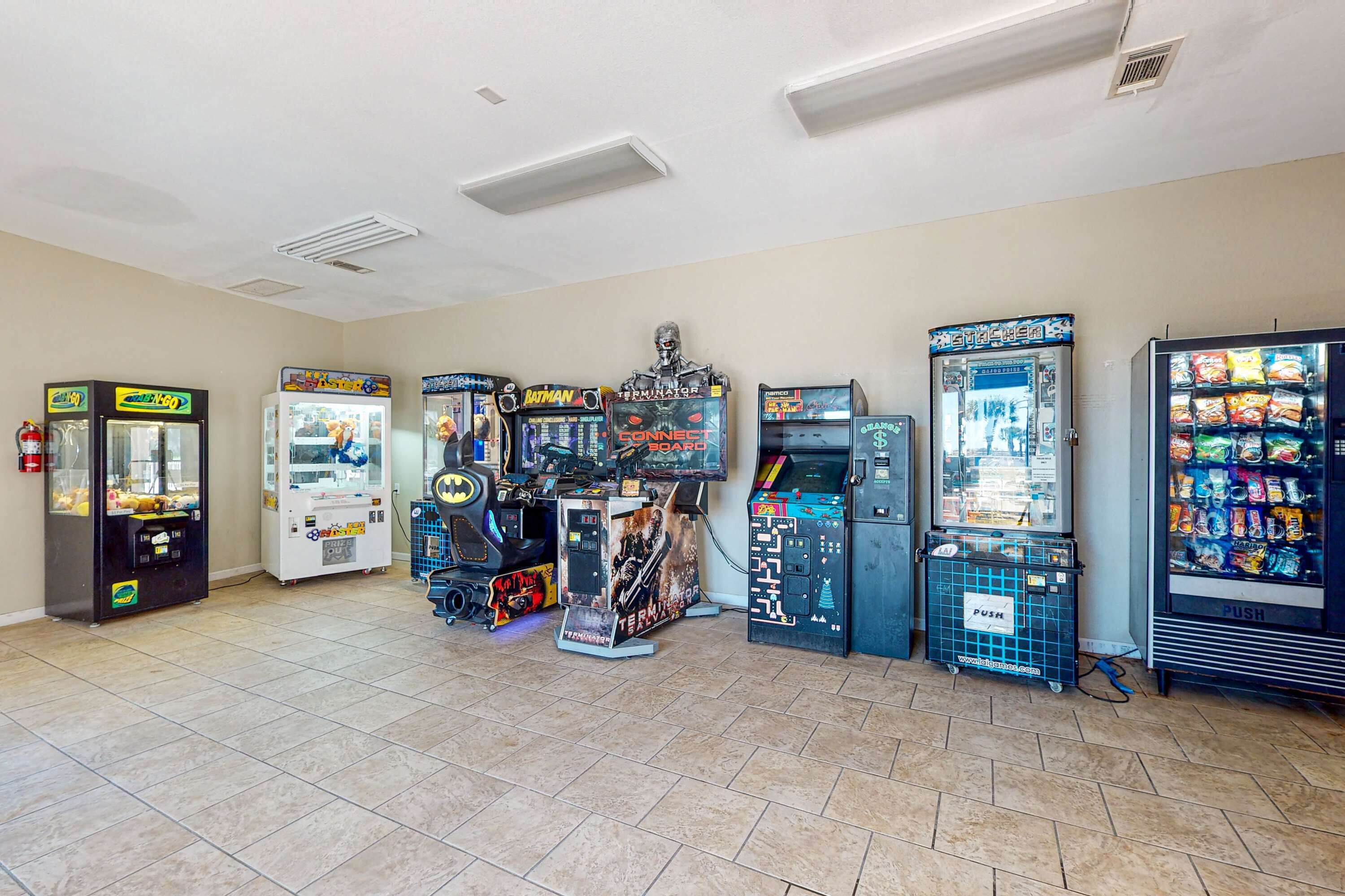 Eine Reihe von Spielautomaten und ein Getränkeautomat in einem Raum mit Fliesenboden und weißen Wänden.