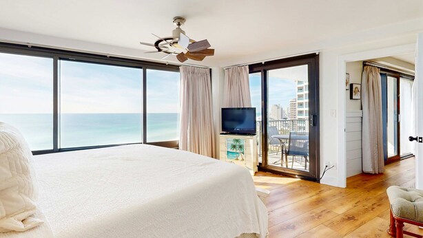 A bedroom with a large bed, a ceiling fan, a TV, and a view of the ocean. - Gulf-front condo with balcony, ocean view, W&D, pool, hot tub & tennis (Miramar Beach)