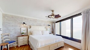 A bedroom with a wooden floor, a large bed, a nightstand, a chair, and a window with curtains. - Gulf-front condo with balcony, ocean view, W&D, pool, hot tub & tennis (Miramar Beach)
