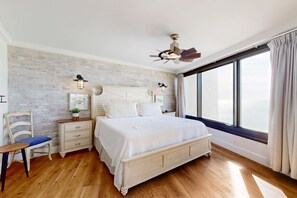 Ein Schlafzimmer mit Holzboden, einem großen Bett, einem Nachttisch, einem Sessel und einem Fenster mit Vorhängen.