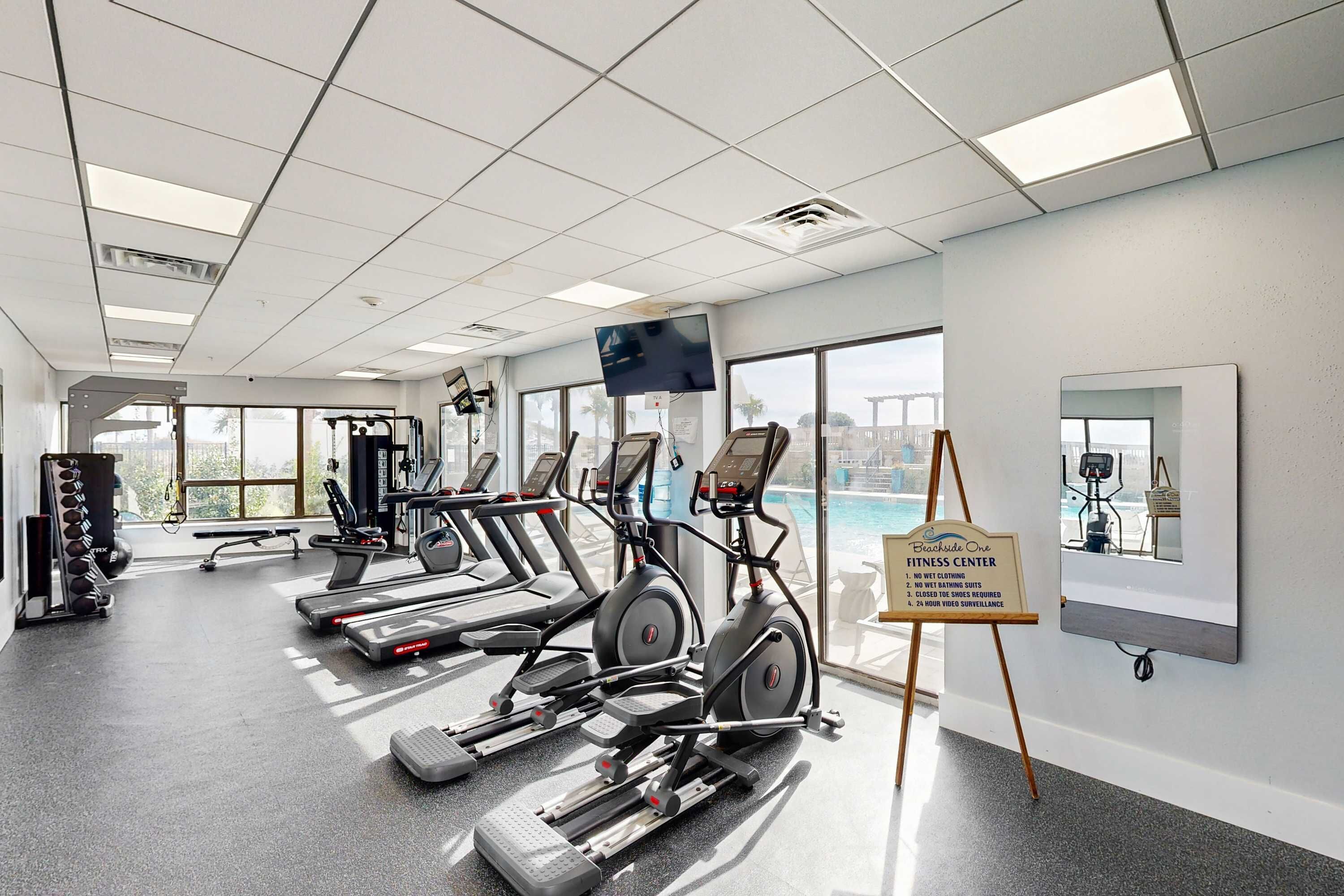 A fitness center with treadmills, elliptical machines, and a weight rack.