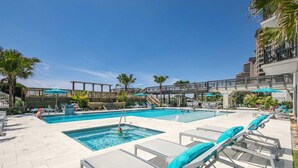 A pool area with multiple swimming pools, lounge chairs, and a wooden bridge connecting different sections. - Gulf-front condo with balcony, ocean view, W&D, pool, hot tub & tennis (Miramar Beach)
