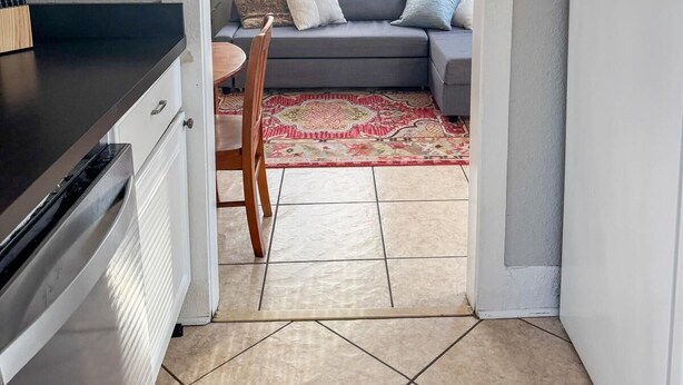 Una cocina con zona de comedor, un sofá gris con cojines estampados y una alfombra roja.