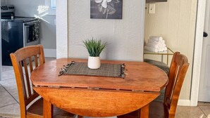 Un comedor con una mesa redonda de madera, dos sillas de madera y dos cuadros de flores colgados en la pared.