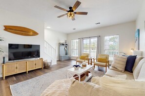 A spacious living room with a large flat-screen TV, a ceiling fan, and a wooden surfboard decoration. - Gorgeous townhouse, plenty of space, family-friendly and close to everything! (Santa Rosa Beach)