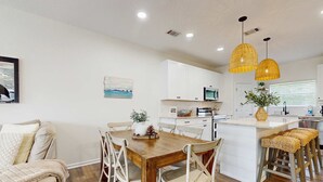 Uma cozinha moderna com armários brancos, uma mesa de jantar de madeira e duas luminárias pendentes amarelas.