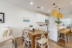 A modern kitchen with white cabinets, a wooden dining table, and two hanging yellow pendant lights. - Gorgeous townhouse, plenty of space, family-friendly and close to everything! (Santa Rosa Beach)