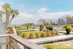 A beachfront property with wooden walkways, palm trees, and a view of the ocean. - Luxury poolside townhouse with deck, balcony, washer/dryer, on-site pool, grill (St. George Island)