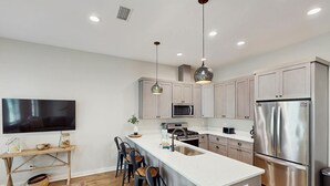 Een moderne keuken met een centraal eiland, roestvrijstalen apparatuur en hanglampen.