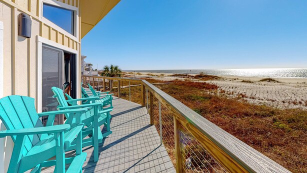 Eine Holzterrasse mit türkisfarbenen Stühlen mit Blick auf einen Strand.