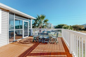 Une terrasse en bois avec une table et des chaises, une balustrade blanche et une vue sur des palmiers et des immeubles.