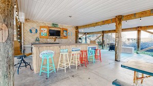 Un área de bar al aire libre con techo de madera, una barra y taburetes de colores.