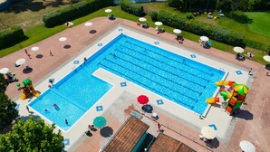 Une grande piscine rectangulaire, divisée en plusieurs couloirs, entourée d’une terrasse dallée agrémentée de parasols et d’espaces aménagés pour s’asseoir.