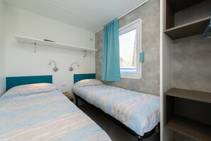 Ein Schlafzimmer mit zwei Einzelbetten, einem Vorhangfenster, einem Regal über den Betten und einem Kleiderschrank.