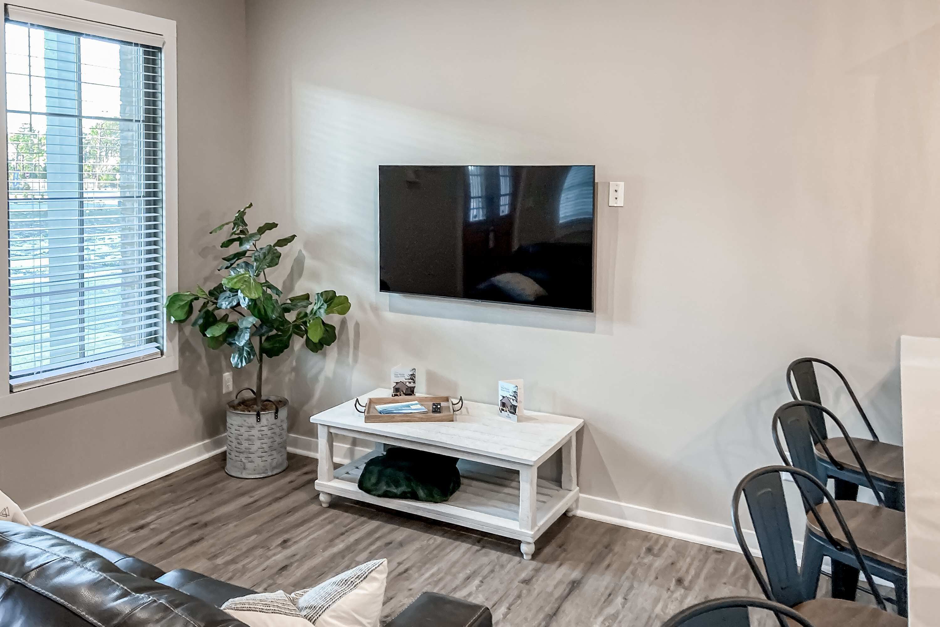 A living room with a TV mounted on the wall, a white coffee table, a green plant, and a leather sofa.