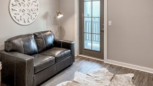 A dark leather sofa with a decorative wall piece and a floor lamp, a large white rug, and a wooden door with a view of a fence. - Dog-friendly abode with a washer/dryer, central AC, & patio - perfect central location (Port St. Joe)