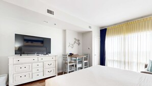 A hotel room with a large bed, a TV mounted on the wall, a desk with chairs, and a window with curtains. - Luau 7012 | 10th-floor studio in Miramar Beach with pool, gym, hot tub, elevator (Miramar Beach)