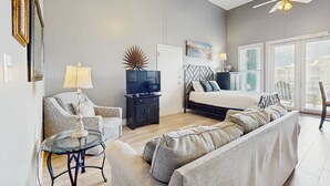 A modern living room with a sofa, a glass coffee table, a TV, and a ceiling fan. - Spacious condo with large living area, private balcony & shared pool (Santa Rosa Beach)