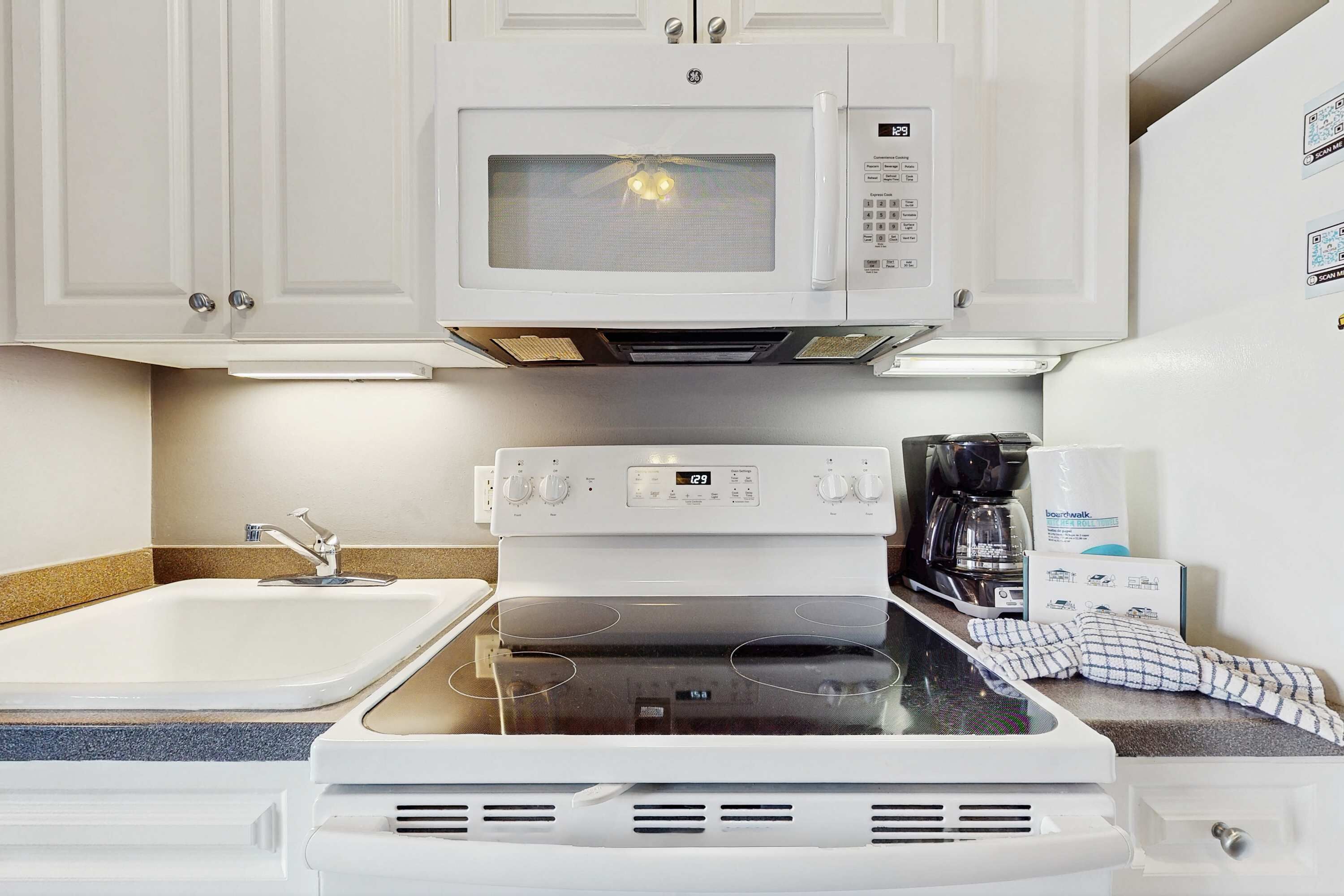 A kitchen with white cabinets, a microwave, an oven, and a coffee maker.
