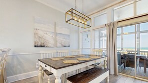 Un comedor con una mesa de madera, sillas blancas y un banco. Hay dos cuadros en la pared y un ventanal con vistas.