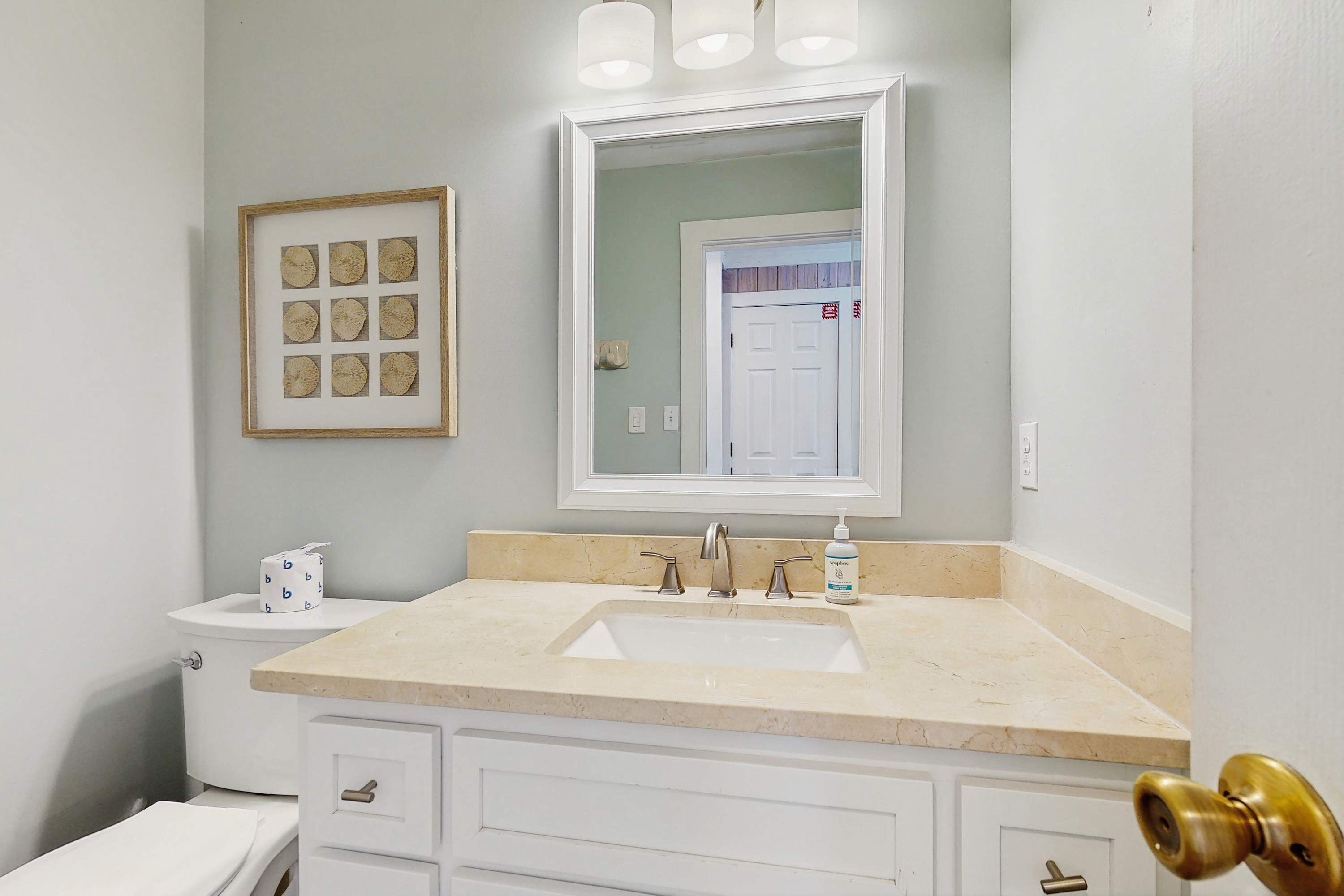 Une salle de bain avec des toilettes blanches, un lavabo doté d’un plan-vasque beige et un miroir au-dessus.