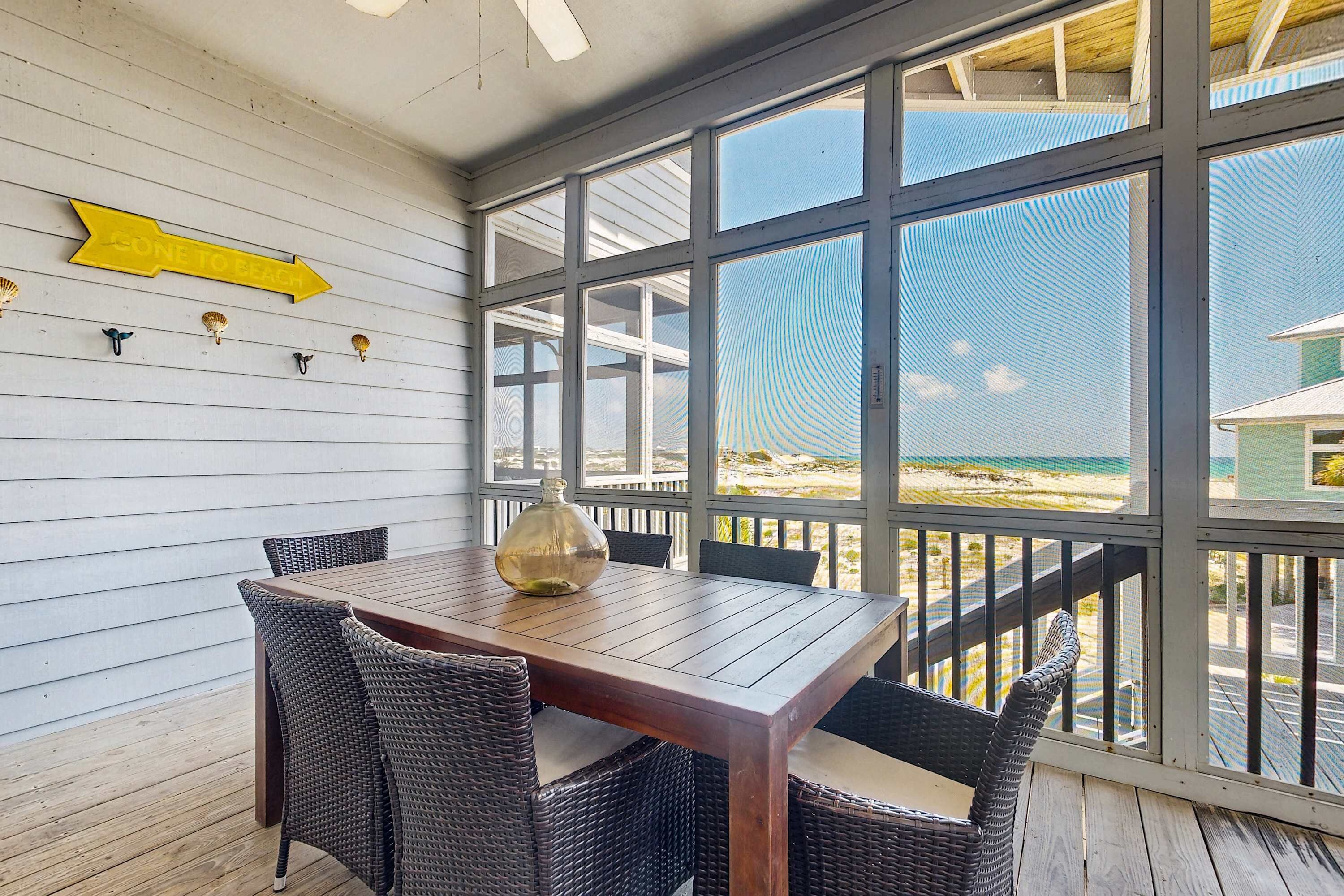A wooden deck with a table and chairs, a yellow directional sign, and a view of the beach.