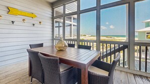 Una terraza de madera con una mesa y sillas, un letrero direccional amarillo y vistas a la playa.