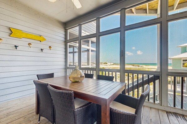 A wooden deck with a table and chairs, a yellow directional sign, and a view of the beach. - Gulf-front duplex with amazing views & screened deck - right on the beach (Santa Rosa Beach)