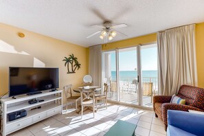 Ein Zimmer mit Fernseher, Deckenventilator, Balkon mit Meerblick und einem gemusterten Sofa.