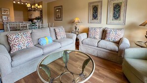 Una sala de estar con dos sofás, una mesa de centro de vidrio y un área de comedor al fondo.