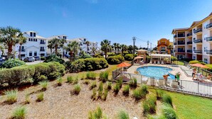 Un resort con piscina central, palmeras y varias edificaciones con balcones.