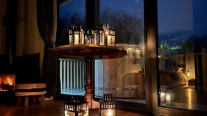 Gemütliche Innenraumgestaltung mit einem Holztisch und Laternen, große Fenster mit Blick ins Freie.