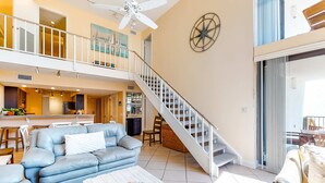 A spacious living area with a blue sofa, a white coffee table, and a staircase leading to an upper level. - Spacious, beachfront home w/ shared outdoor pool, hot tub, & beach access (Miramar Beach)