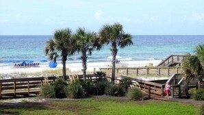 A beach view with a wooden boardwalk, palm trees, and a person walking. - Spacious, beachfront home w/ shared outdoor pool, hot tub, & beach access (Miramar Beach)