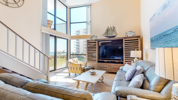 A spacious living room with a large TV, leather sofas, a coffee table, and a balcony with a view of the city. - Spacious, beachfront home w/ shared outdoor pool, hot tub, & beach access (Miramar Beach)