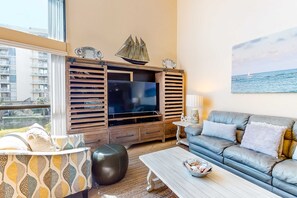 Ein modernes Wohnzimmer mit großem Fernseher, einer Couch, einem Couchtisch und Meerblick durch das Fenster.