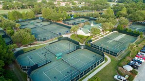 Une vue aérienne d’un complexe sportif comprenant plusieurs courts de tennis, entouré d’arbres et doté d’un parking.