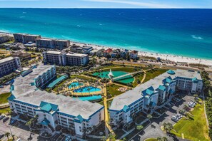 Une vue aérienne d’un complexe hôtelier comprenant plusieurs bâtiments, un espace piscine central et une plage.