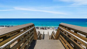 A wooden boardwalk leading to a beach with clear blue water and a few people in the distance. - Big 'O Beach Miramar/Destin (Miramar Beach)